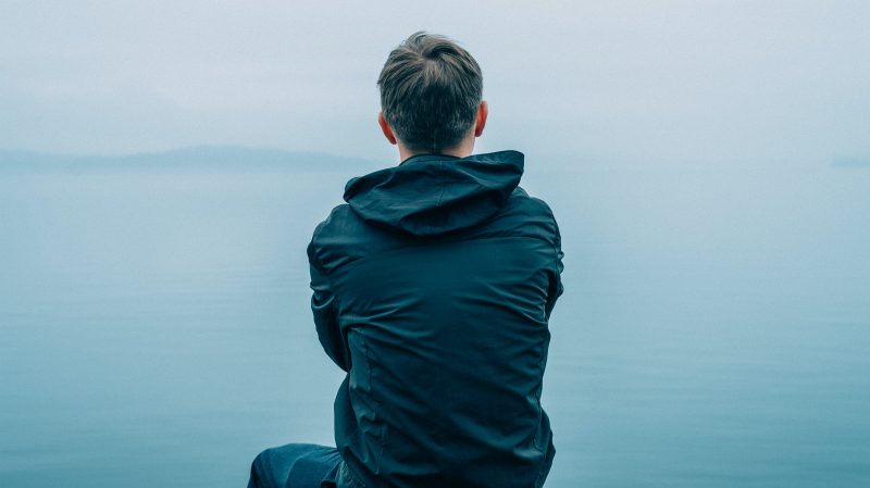 Sad guy sitting at water's edge